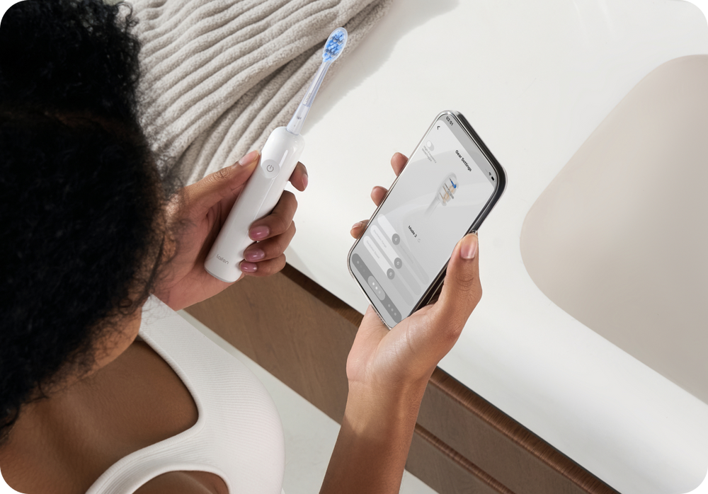 Illustration of a person using a smart electric toothbrush with a phone app in a bathroom.
