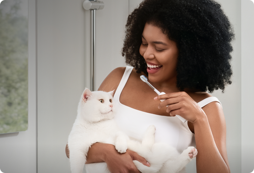 Woman brushing a cat's teeth in a bathroom setting