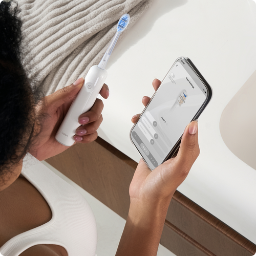 Illustration of a person using a smartphone with an electric toothbrush in hand.